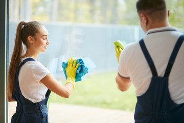 Cleaning service concept. Rear view on two workers of cleaning company washing panoramic window together. Joint work, having conversation, speak