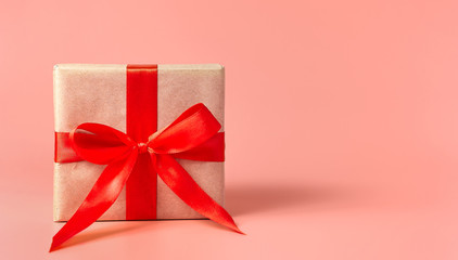 Christmas gift with red ribbon isolated on a pastel pink background. Christmas present background with copy space.