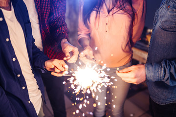 Group of happy people holding sparklers at party and smiling. Young people celebrating New Year together. Friends lit sparklers. Friends enjoying with sparklers in evening. Blur Background.