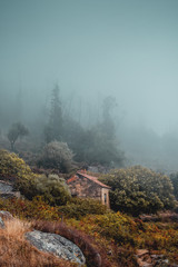 A stone old and remote hut in the wild mountain landscape with heavy weather fog of low hanging clouds at the hillside. Serra de Monchique, Algarve in Portugal