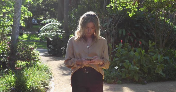 Young woman walking through garden on her mobile phone_slow motion