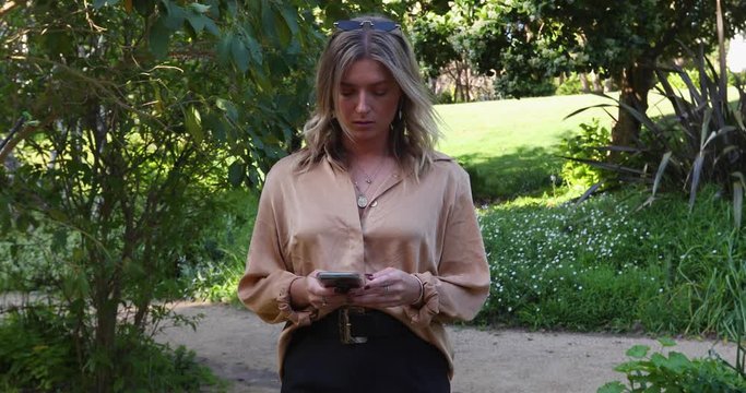 Young woman walking through garden on her mobile phone_slow motion
