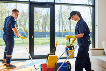 Two janitors clean country house with panoramic window, wash floors. Side view on process of working