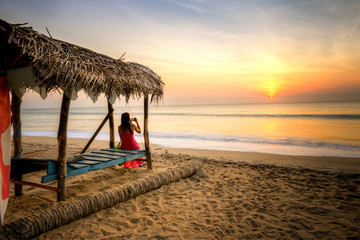 femme en rouge photographie un couché de soleil sur une plage de Arugam Bay au Sri lanka