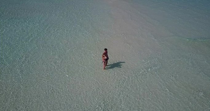 white sandbank surrounded by crystal clear water and lovely romantic couple walking at the sandbar in Canradaman island in Balabac, Palawan, Philippines