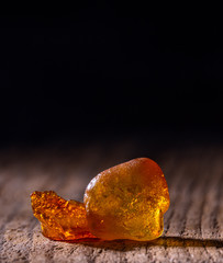 Natural amber. A piece of yellow transparent natural amber on large piece of dark stoned wood.
