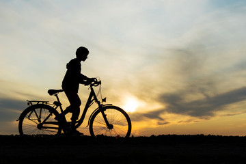 Fototapeta na wymiar Boy , kid 10 years old riding bike in countryside, silhouette of riding person at sunset in nature
