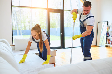 Two person in blue uniform, cleaning equipment, wearing yellow rubber gloves mop floor, preparing new sofa for tenants of new house