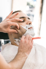 Obraz na płótnie Canvas Hairdresser shaves a beard to a man with a razor in the barbershop