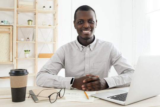 African male sitting at desk in his office smiling happily while looking at camera