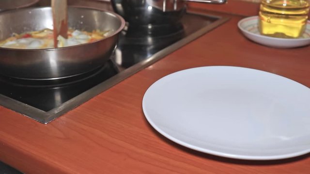 A chef puts a steaming omelet, scrumbled eggs with tomatoes and onion in a plate close up