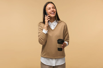 Portrait of young woman in brown pullover looking aside and smile while talking on phone, isolated...