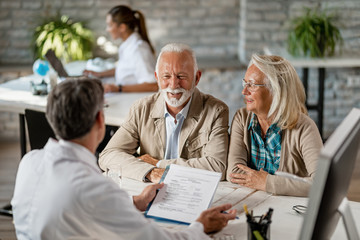 Happy mature couple talking to a doctor while going through their medical reports. - obrazy, fototapety, plakaty