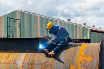 The welder is welding a steel structure with the process Flux Cored Arc Welding (FCAW) in Industrial factory.