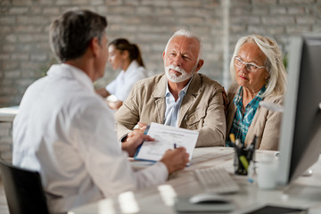 Mature couple planning their health insurance policy with a doctor at clinic.