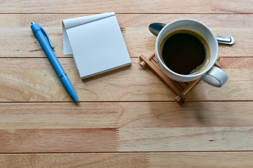 Coffee cup, blank notebook and pen on wood table