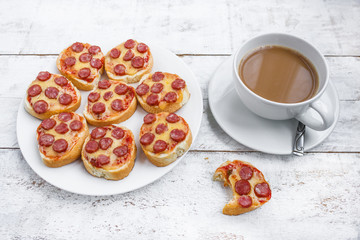 homemade mini pizza sandwiches with hunting sausage cheeese round bread on plate cup of coffee on white table