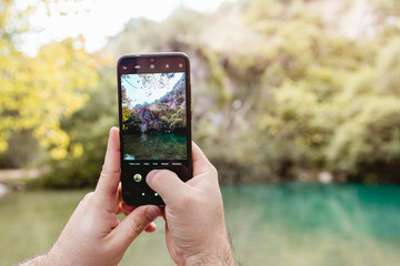 Person hands taking a picture with a mobile phone of the nature at the river