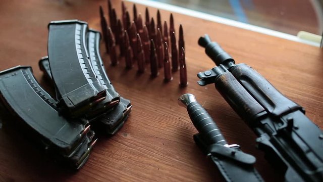 The hand of a soldier or a terrorist puts ammo on the table.