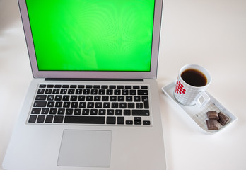 Fototapeta premium Laptop computer with blank green screen with coffee cup on white table background.