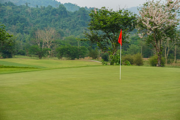 Obraz premium Red flag on Green Golf Course and Green Mountain.
