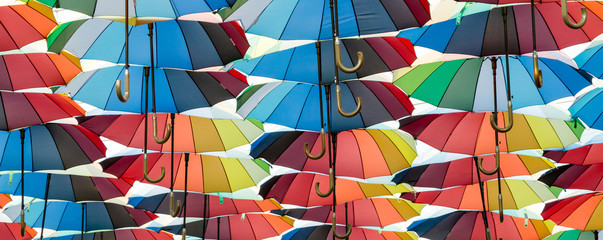 a collection of open umbrellas floating in the air, each umbrella painted in all colors of the rainbow, photographed from the side
