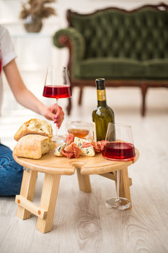 A folding table is on the floor, a green sofa, the girl’s hand holds a glass of red wine in two glasses, blue cheese, camembert, brie, jamon, ciabata, surprise, breakfast in bed, gift, birthday