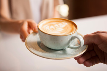 Cropped close up of a woman taking cup of delicious coffee from barista. Professional barista handing coffee cup to female customer