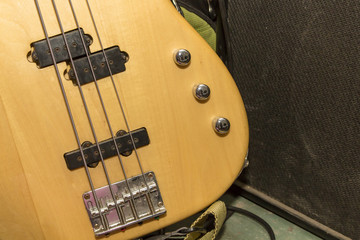The lower part of the body of a four-string bass guitar on the background of the subwoofer