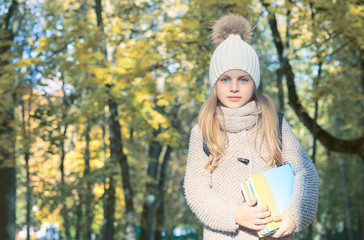 Portrait of teenage smiling schoolgirl girl in autumn park. Student is holding books and notebook in her hands.