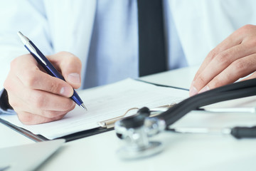Mid section of male doctor writing write prescription to patient at worktable. Panacea and life...