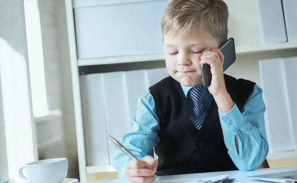 Boss boy making notes and talks on the phone sitting at the desk with laptop in office.