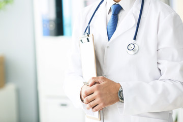 Close-up of clipboard with blank paper in medical doctor hand. Male doctor listens to the patient holding a clipboard with documents for hospitalization.