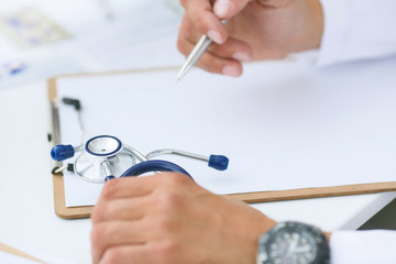 Male doctor on duty in white coat reading patient's information with pen in hand, filling prescription or checklist document close-up. Health and medical concept.