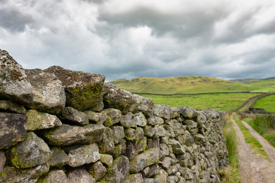 Shallow focus of a dry stone wall seen from the edge of an old, dirt track and bridleway in the heart of the Yorkshire Dales.