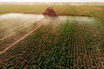 Tractor spraying fertilizer or pesticides on field with sprayer - obrazy, fototapety, plakaty