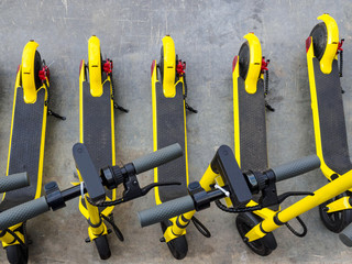 Several yellow e-scooters stand in a row for rent. Scooters are available for rent. Walk around the city light