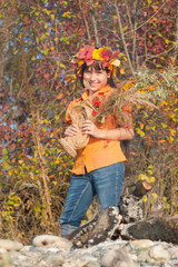 Girl in a wreath of autumn leaves with a bouquet in her hands. Girl in a wreath of yellow leaves with a bouquet of autumn gifts in her hands on a background of autumn foliage