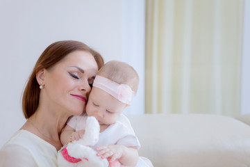 Cute baby in a tender embrace of mother at home