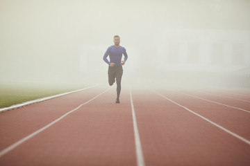 Fototapeta na wymiar A young athlete runs on a stadium in the fog.
