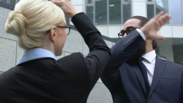 Woman and man in formalwear making high-five gesture, celebrating success, deal