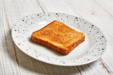 Toasted white toast on a plate on a light wooden background.
