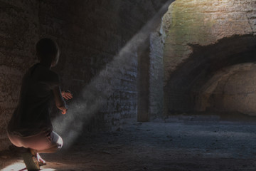 A woman in a dark cave illuminated by a ray of light.
