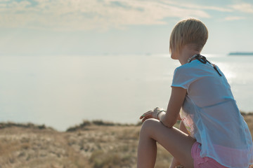 A woman is sitting on a rock near the sea.