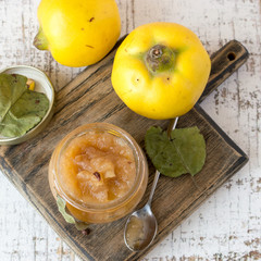 Homemade jam in glass jar and fresh fruit quince on an old table. Selective focus.