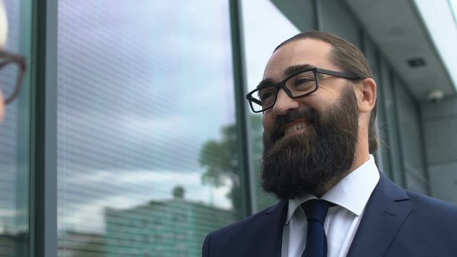 Happy bearded businessman looking at female colleague, discussing successful job
