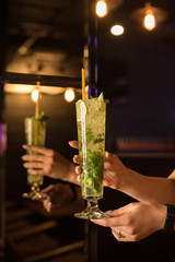 Tall, long glass with mojito, lime green mint, alcohol, crushed ice, hands of the waiter, girls, reflected in the mirror, mohito