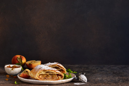 Apple strudel with cinnamon, nuts and and raisins on a dark concrete background.