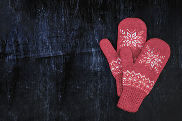 a pair of red-pink-lilac-magenta purple knitted mittens on a dark blue-green-brown wooden
