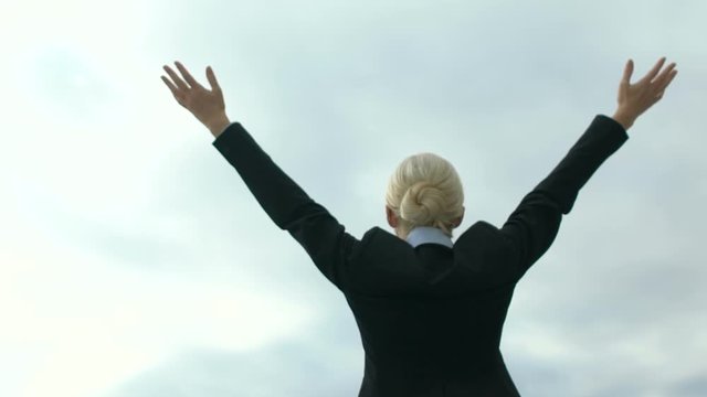 Female in business suit raising hands in victory gesture on sky background, free